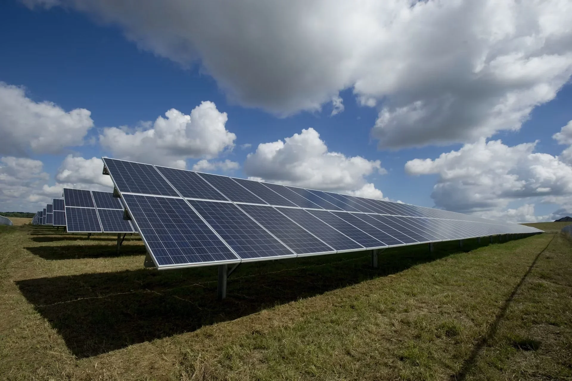 Painéis solares em um campo sob céu azul com nuvens brancas
